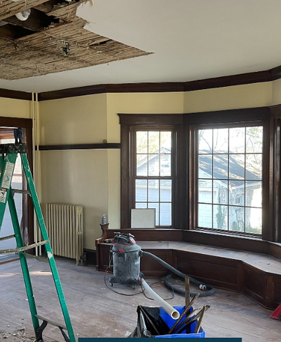 The room before: ceiling opened up, dark trim, a ladder and a shop vac on the floor