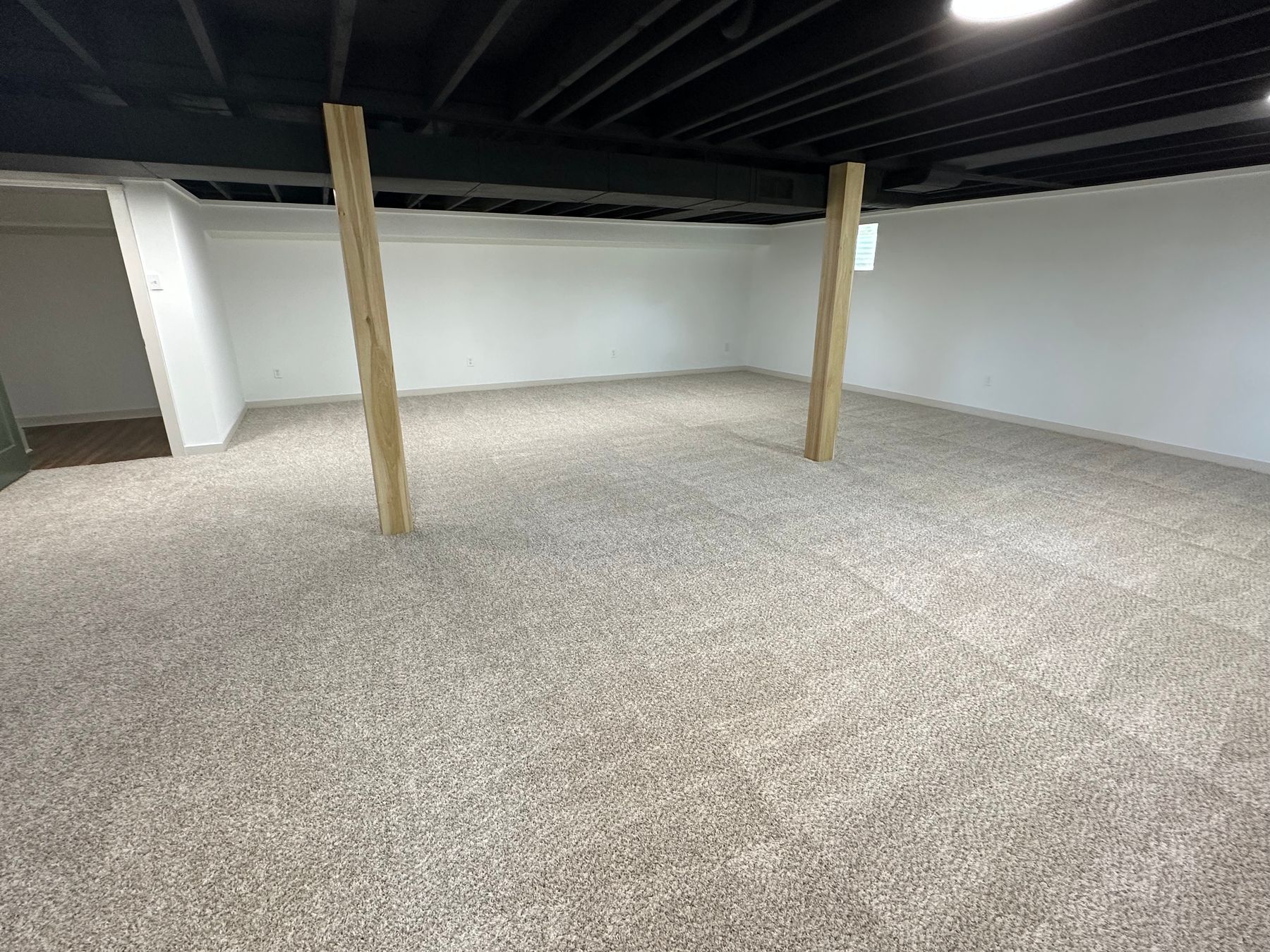 A finished lower level with a painted black ceiling and open joists