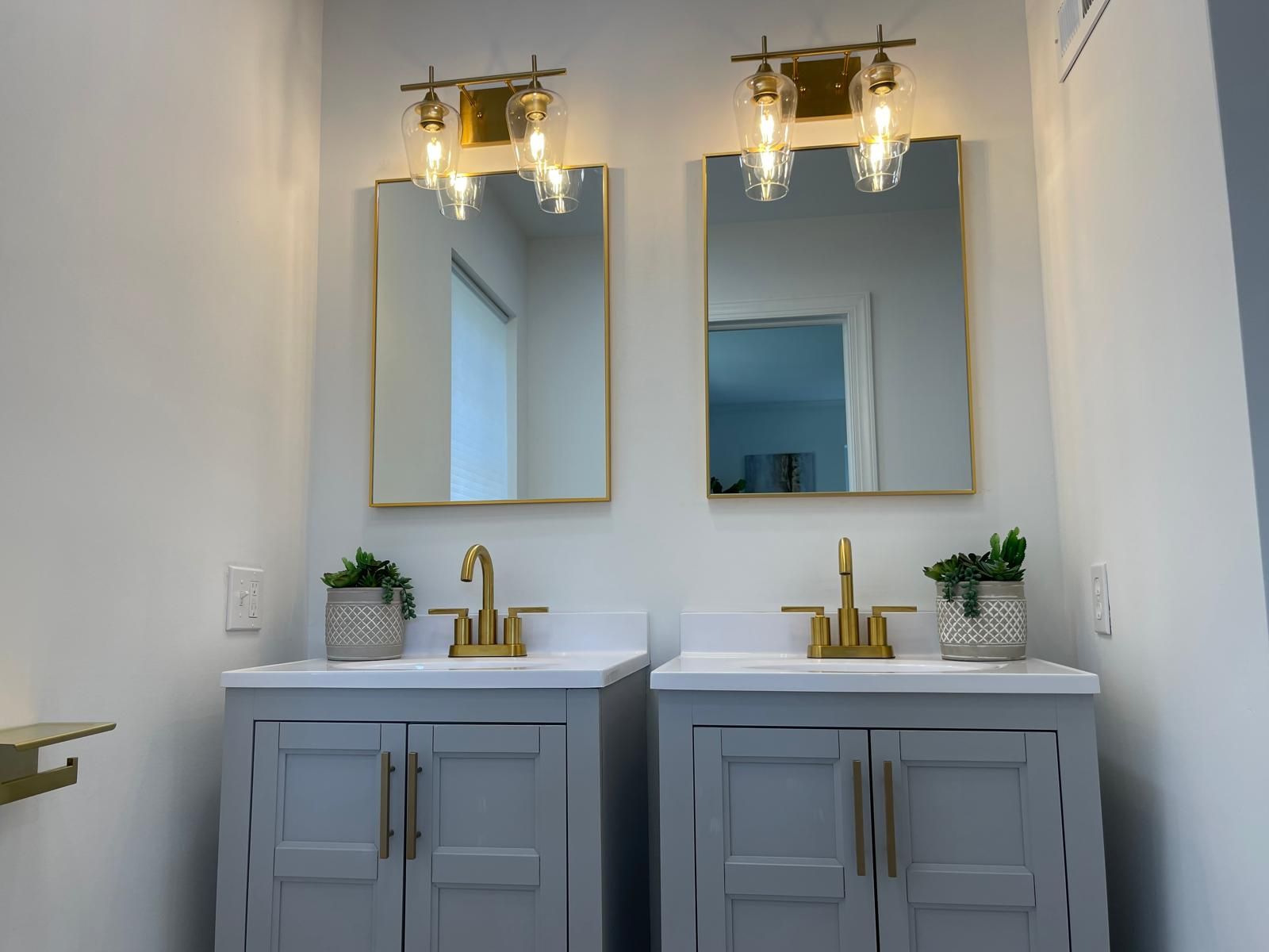 Twin gray vanities with gold sconces and mirrors