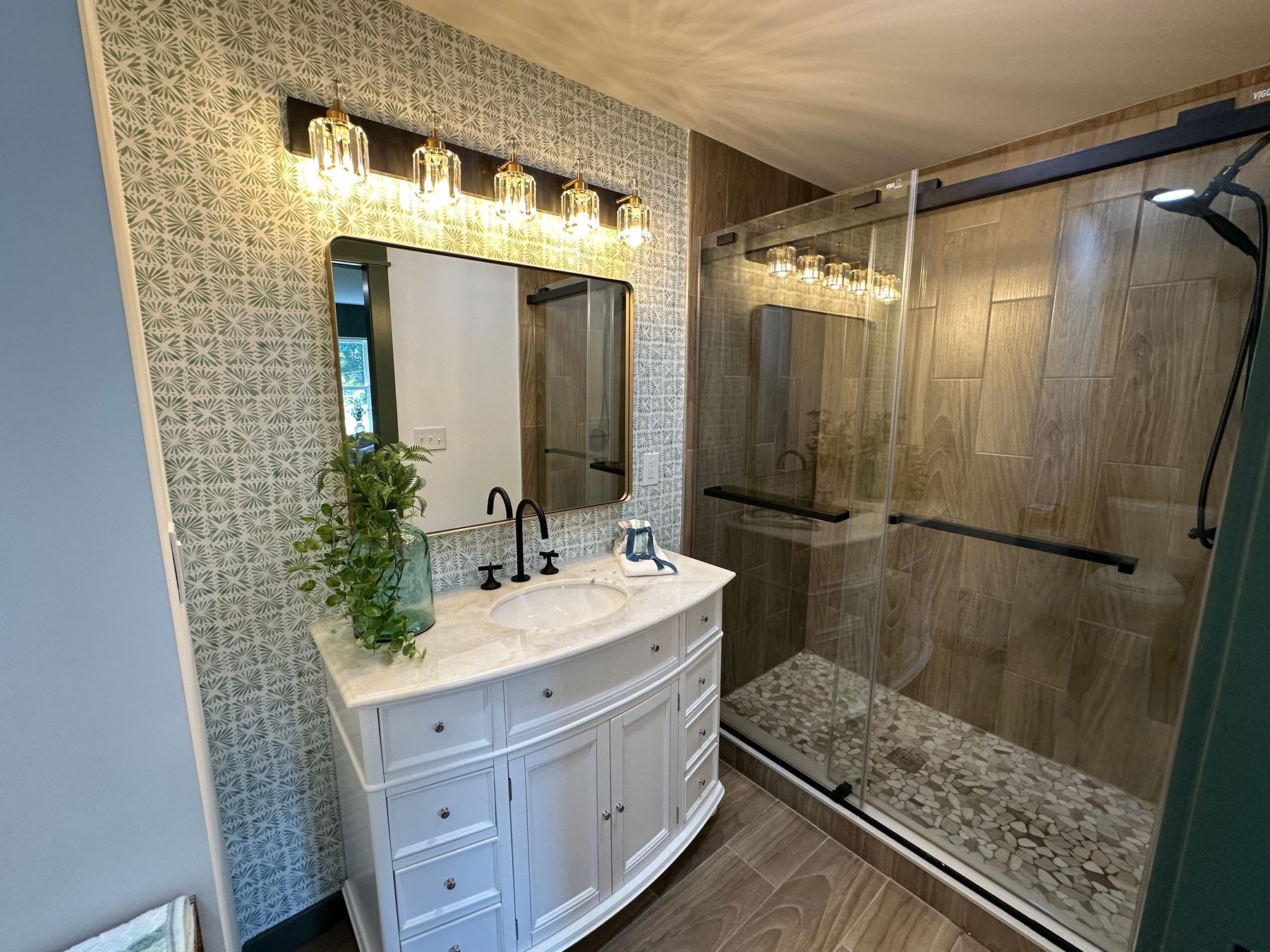 A patterned wall behind a vanity, wood-look tile in the shower