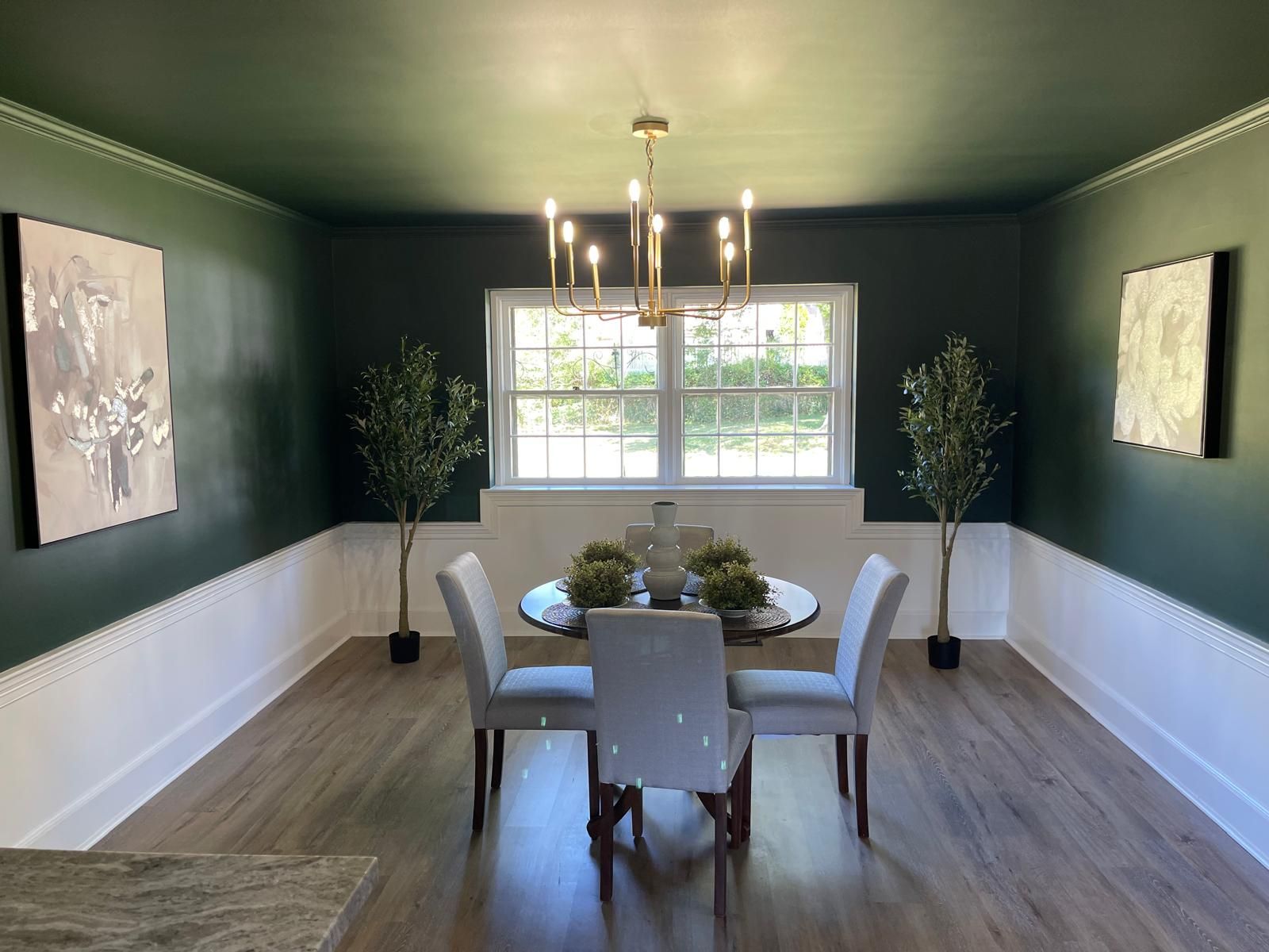 A dining room painted deep green with a brass chandelier