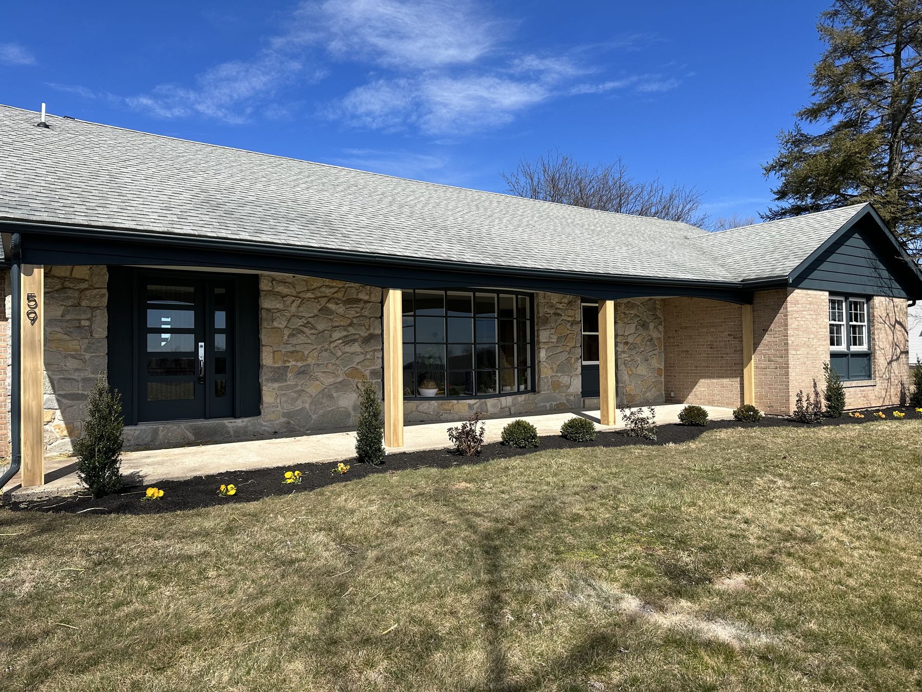 A stone ranch with black windows and new landscaping