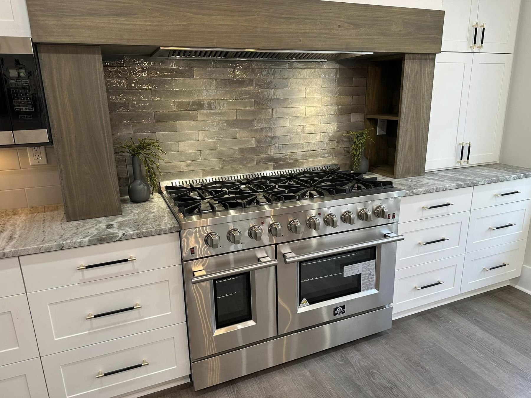 A gas range under a wood hood with a dark stone backsplash